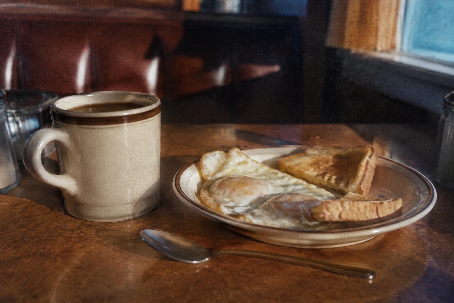 A ceramic coffee cup and fried eggs on a sunlit Formica table.