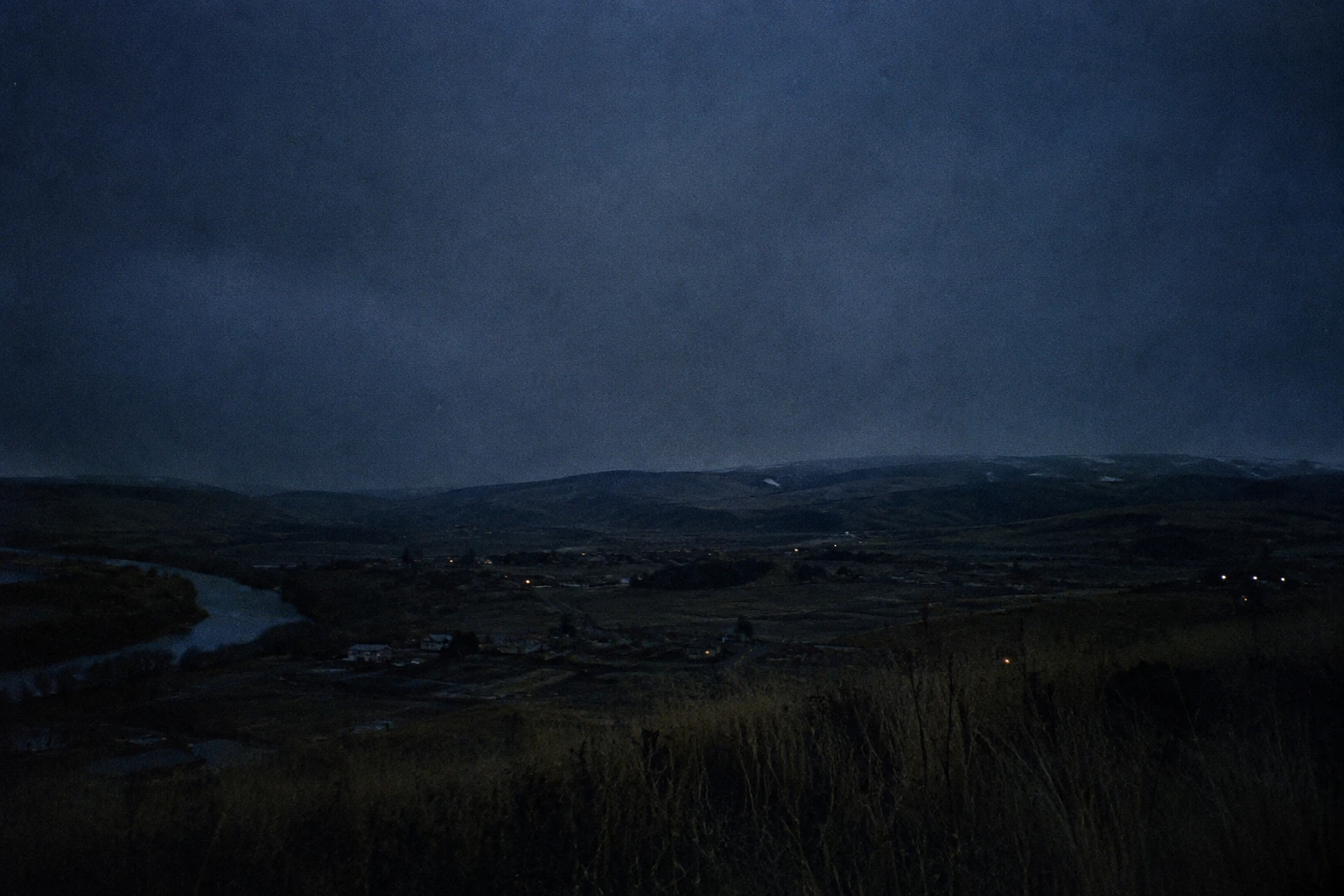 A broad valley, river, and scattered town lights in deep blue darkness.
