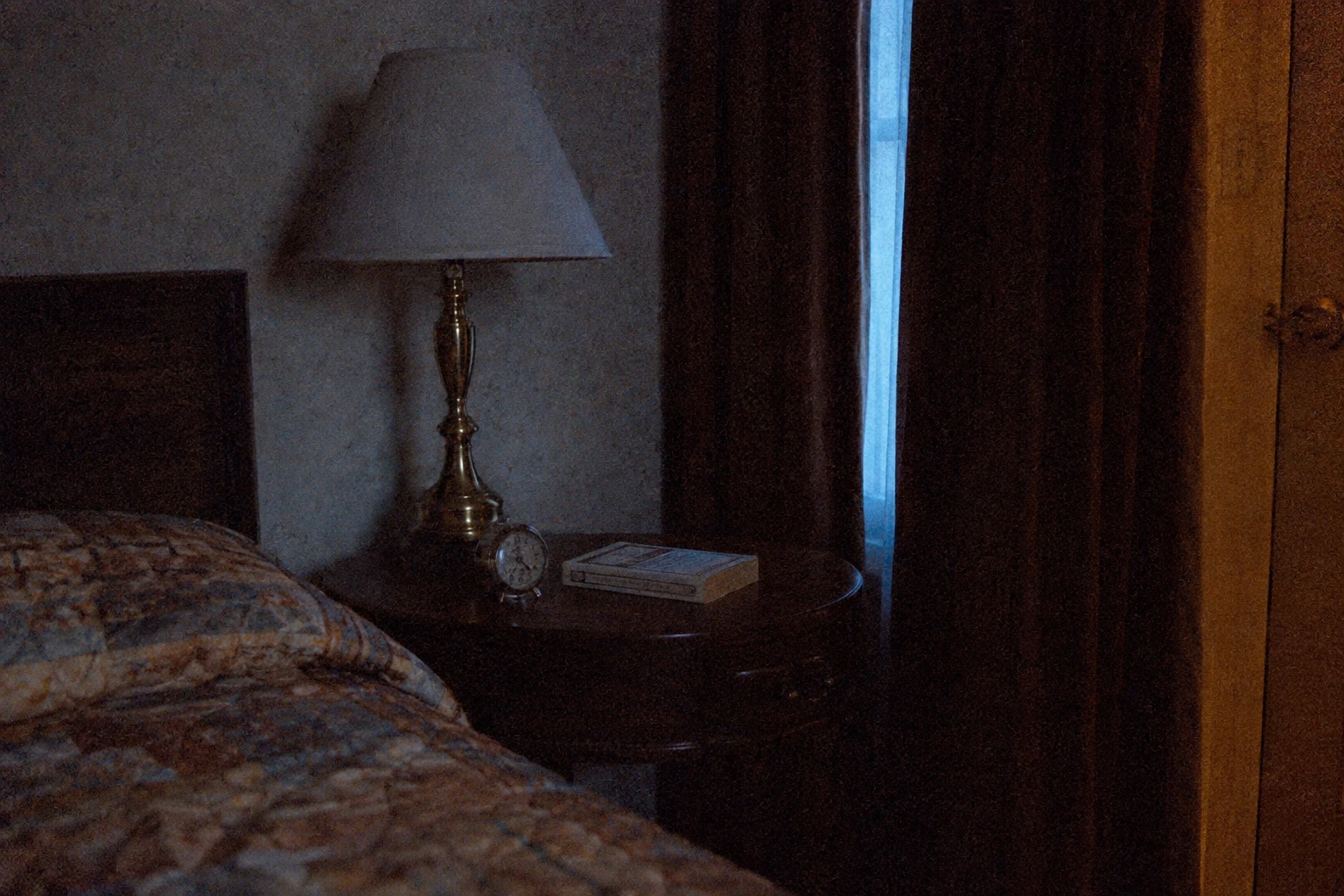 A small analog alarm clock and lamp on a hotel bedside table before dawn.