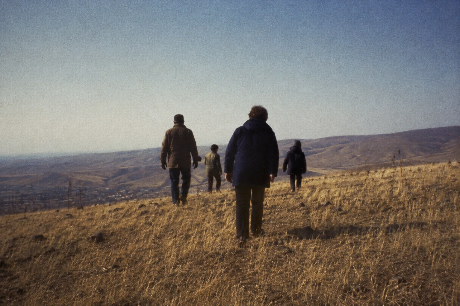 People in muted winter coats walking up a dry grassy Washington hill.